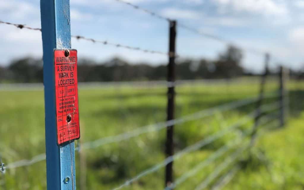 red warning sign reads a survey mark is located on the left in a field along a boundary line